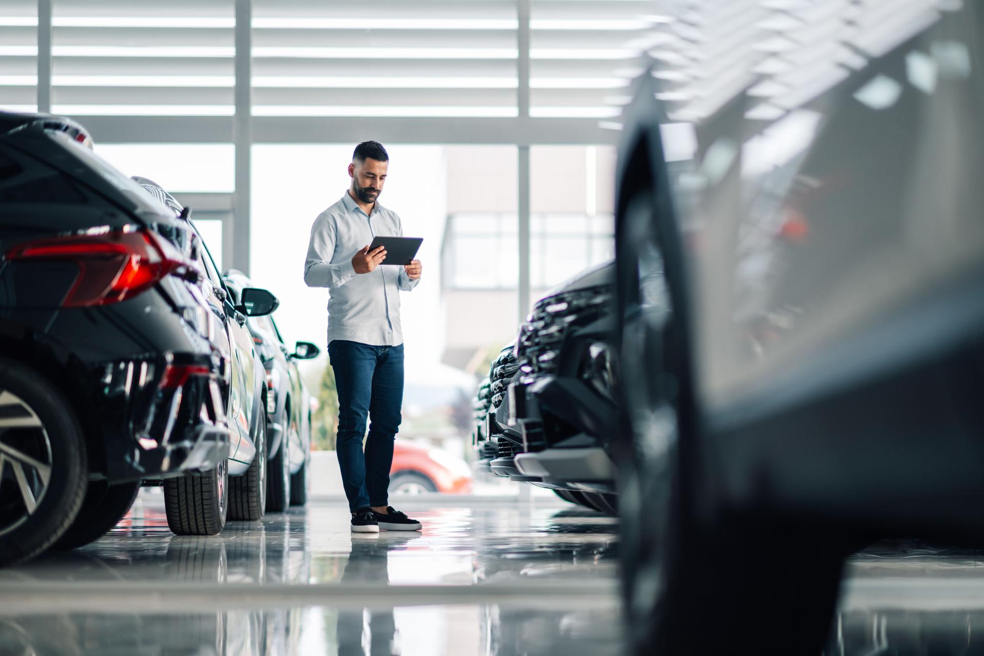 Car salesman using digital tablet while inspecting vehicles in dealership