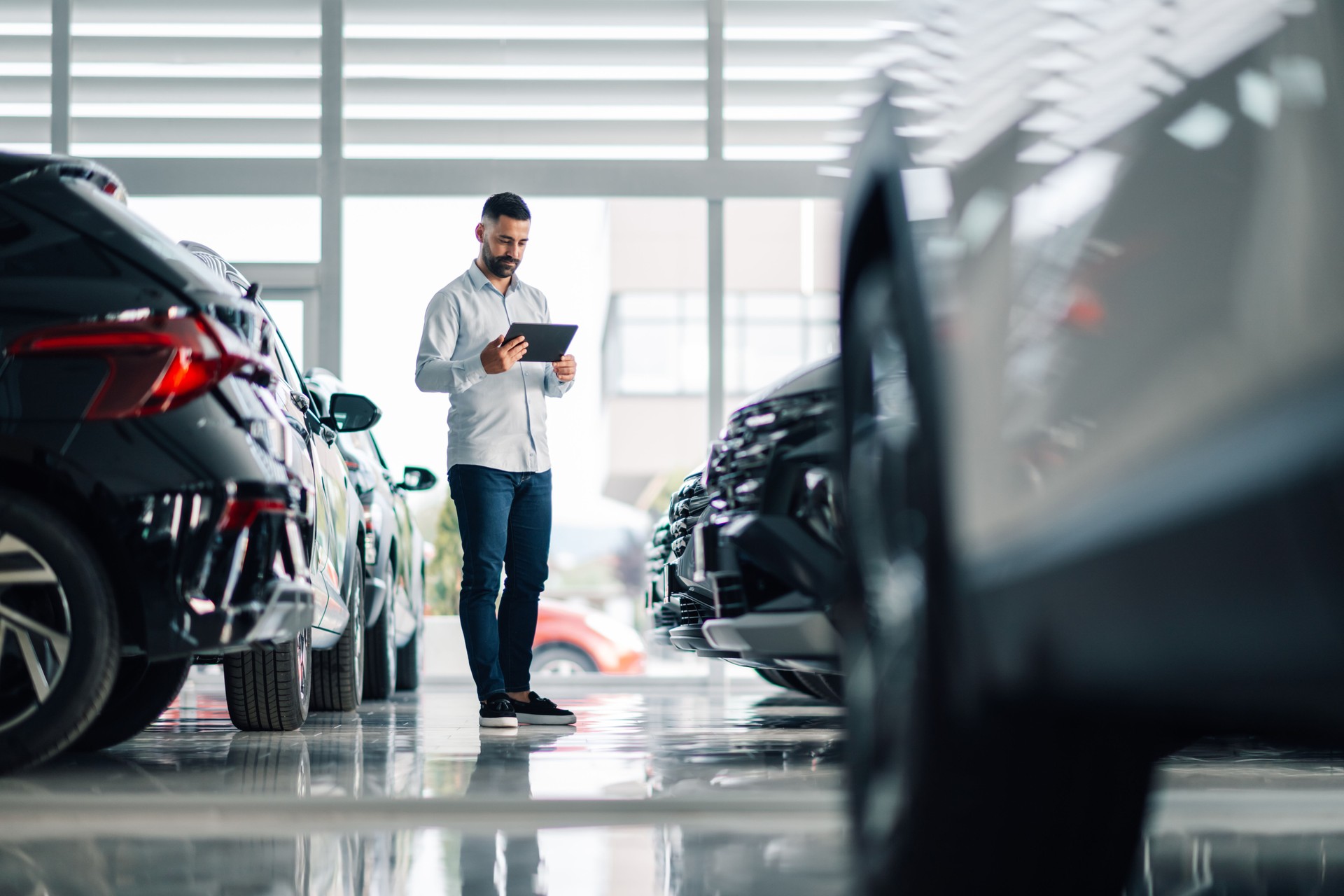 Car salesman using digital tablet while inspecting vehicles in dealership