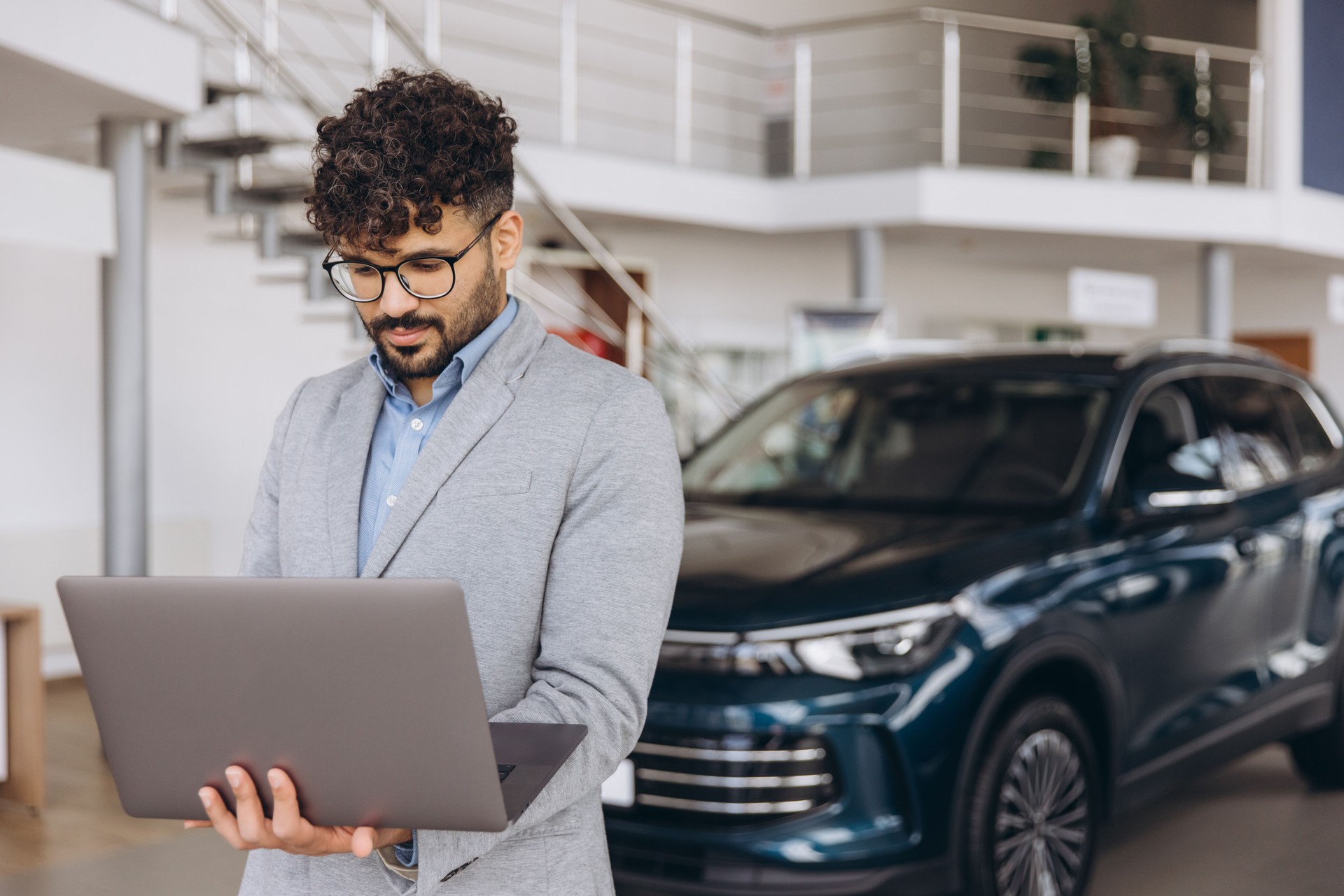 Car salesman working on laptop in car dealership showroom