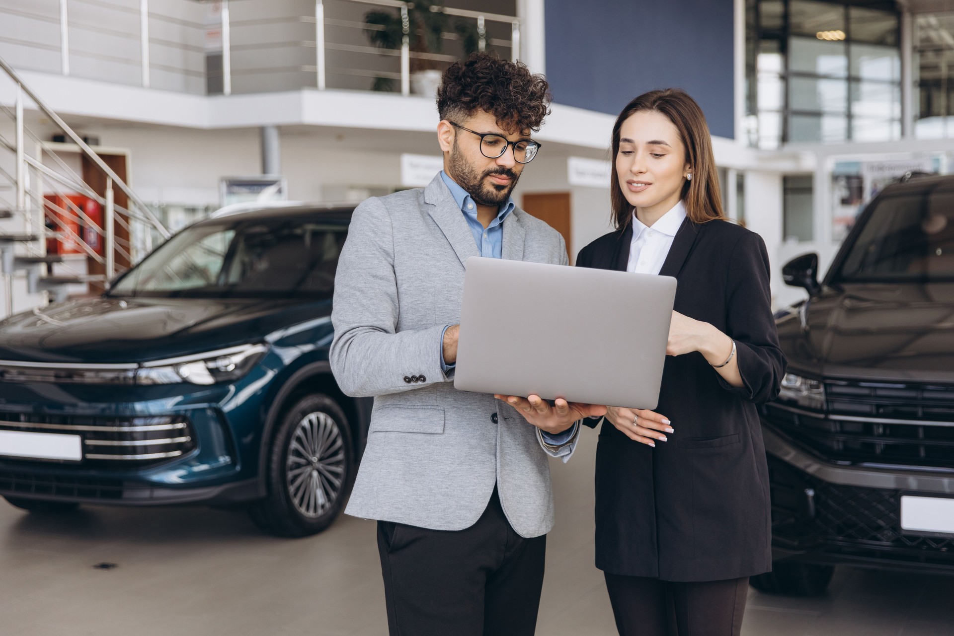 Car dealer showing vehicles to a customer using a laptop in a showroom